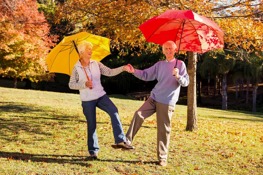 Un cuplu senior dansează sub umbrele colorate și sunt foarte fericiți, așa să iubești vârsta.