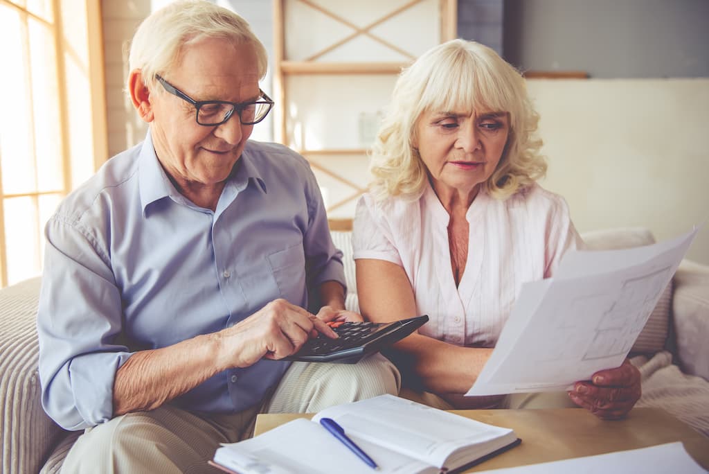 Plan pentru pensionarea Dvs. - un cuplu senior stau la masă și fac niște calcule.