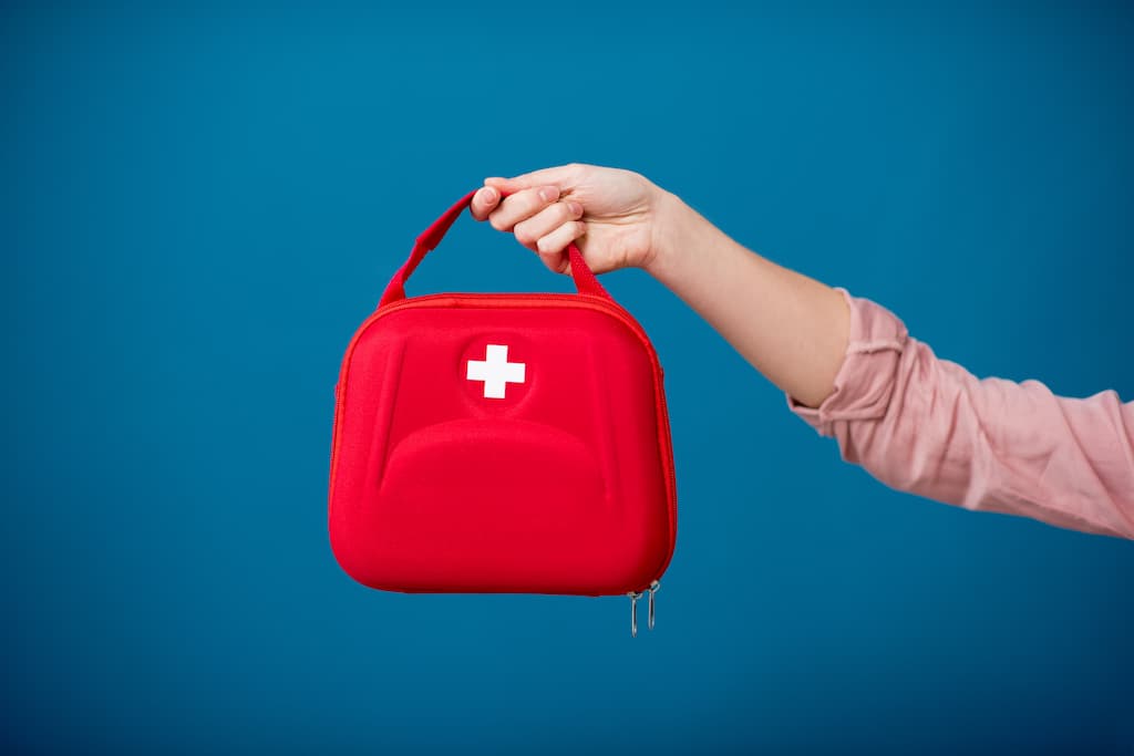 Trusa de medicamente roșu ținut de o mână femeiesc roz pe fundal albastru.