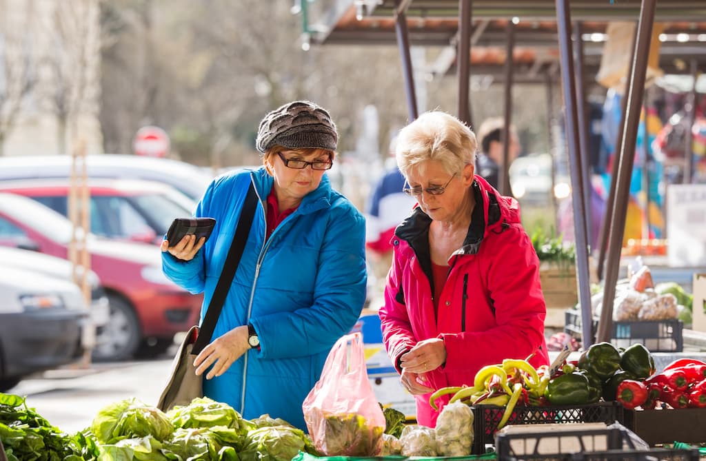 Două femei în vârstă cumpără legume în piață pentru o dietă sănătoasă.