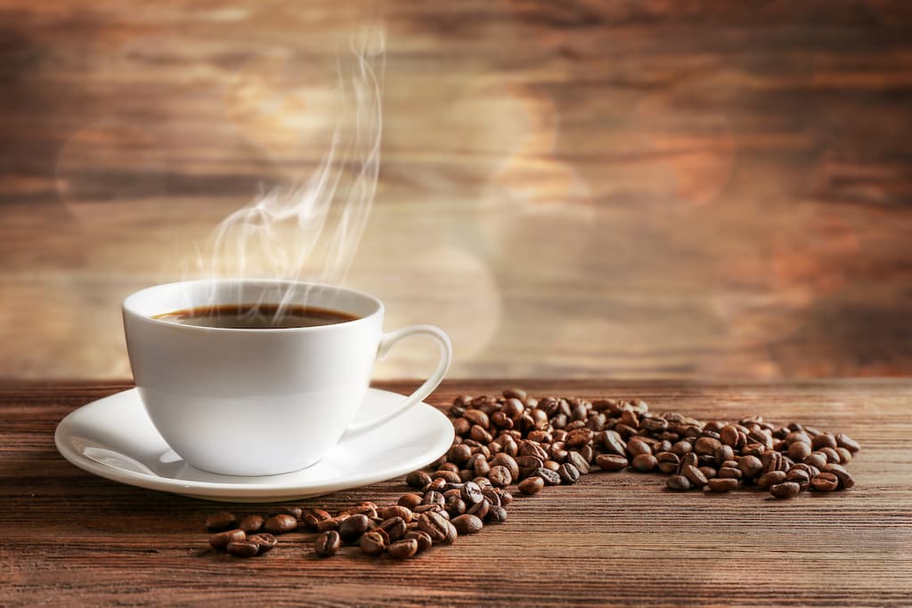 Cafeaua fierbinte este servită într-o ceașcă albă lângă boabe de cafea.